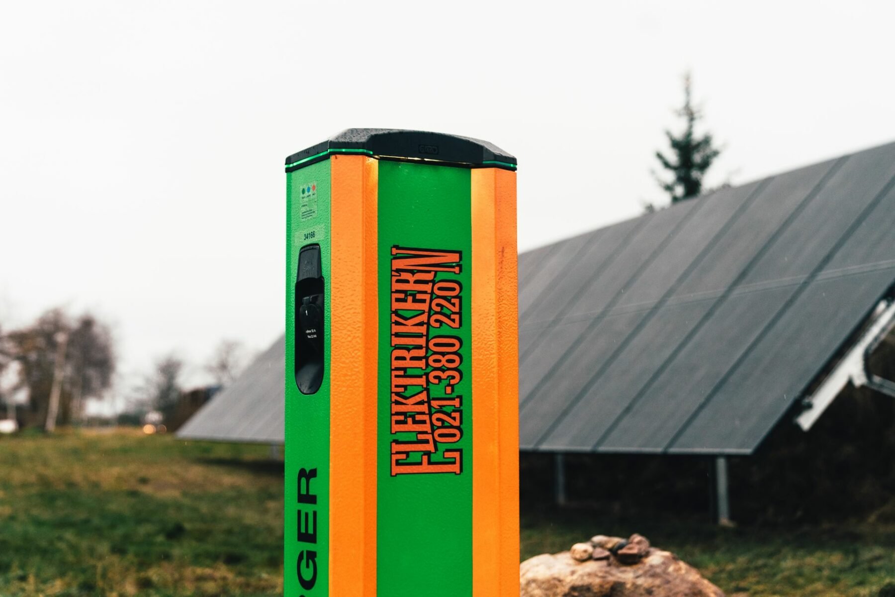 laddstolpe med loggan Elektrikern på som står utomhus med solpaneler i bakgrunden